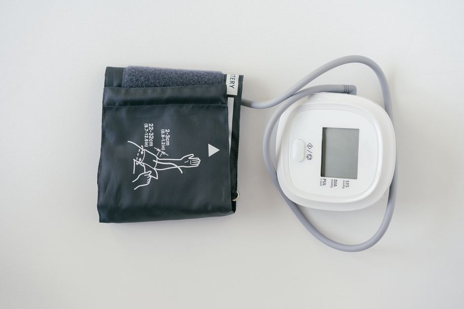 Person checking blood pressure with a monitor while holding oxycodone medication bottle