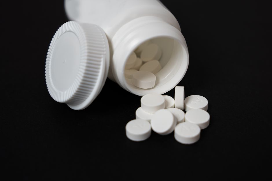 Person holding jaw in pain with pills and glass of water on table representing oxycodone for dental pain relief