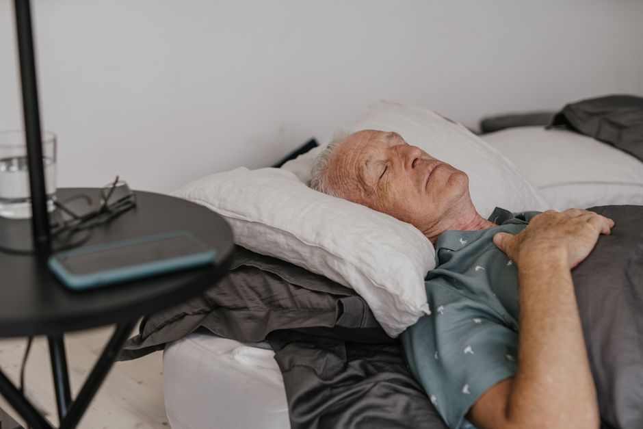 Person sleeping in bed with a glass of water and medication bottle on the nightstand, illustrating oxycodone-induced drowsiness