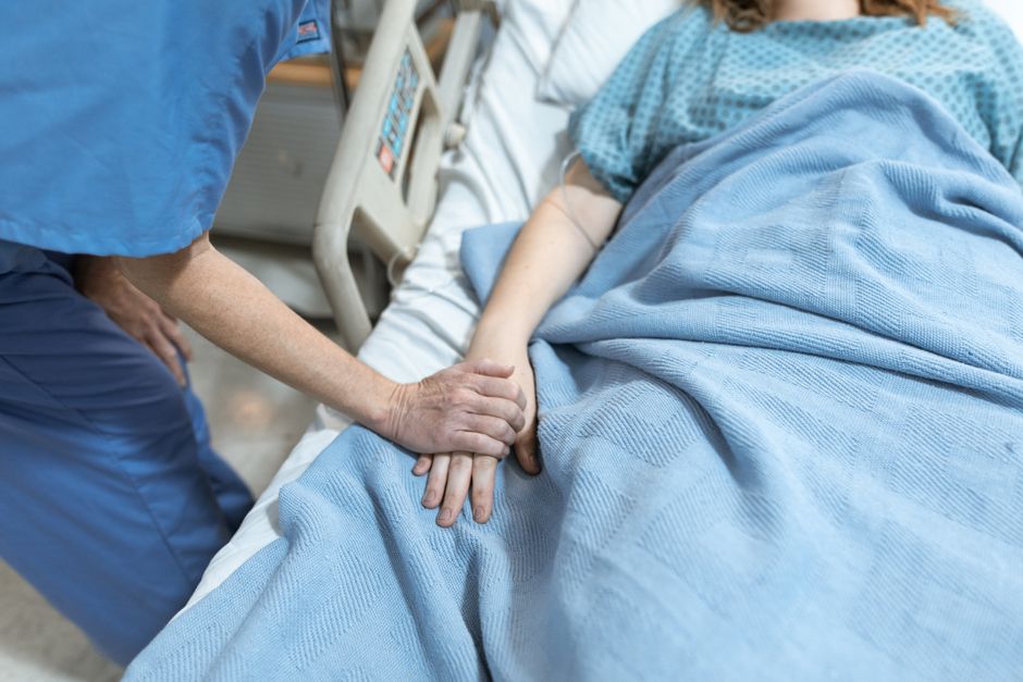 Patient resting in bed after surgery holding a glass of water next to hydrocodone medication