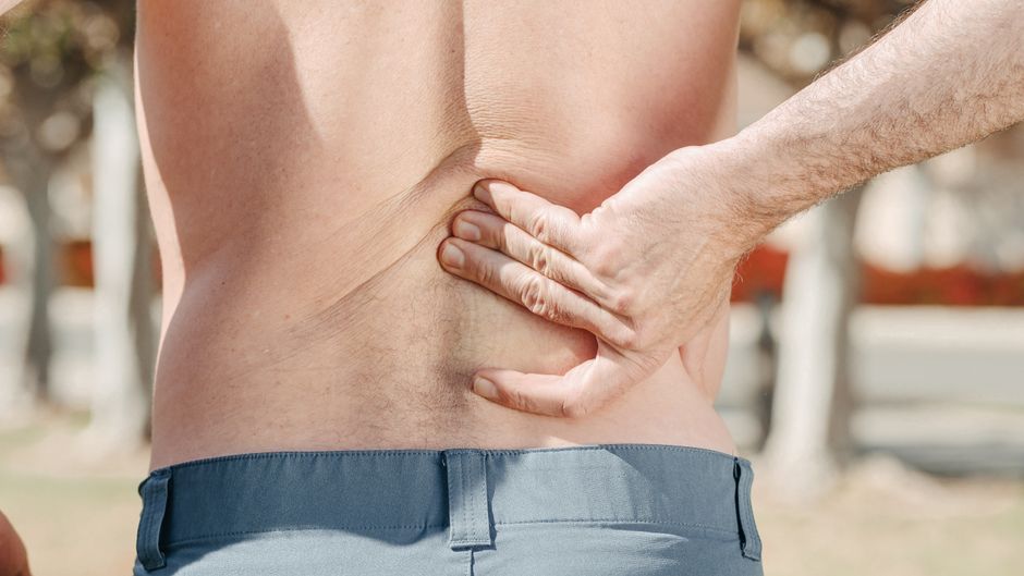 Person holding lower back in pain from kidney stones before taking hydrocodone for relief