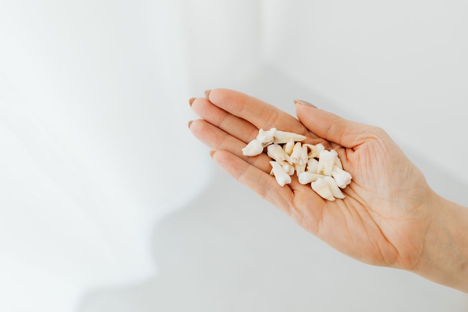 Person resting at home holding a glass of water and pain medication after wisdom teeth removal